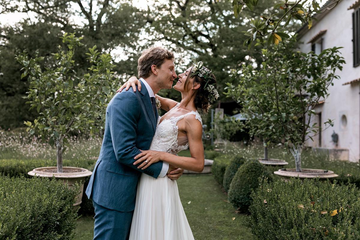 Fotografo per matrimonio Sposi che si abbracciano romanticamente in un giardino curato, con dettagli floreali.