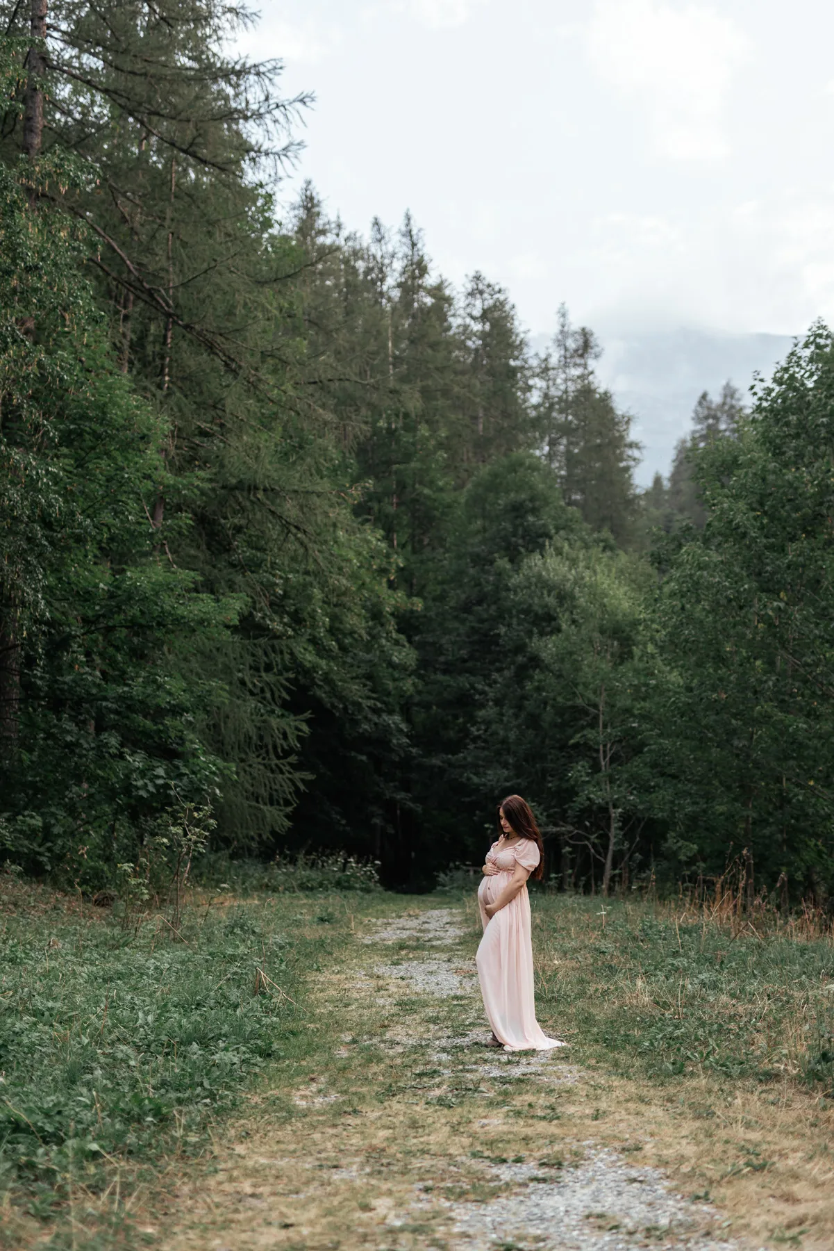 Donna in gravidanza con abito chiaro fotografata su un sentiero nel bosco