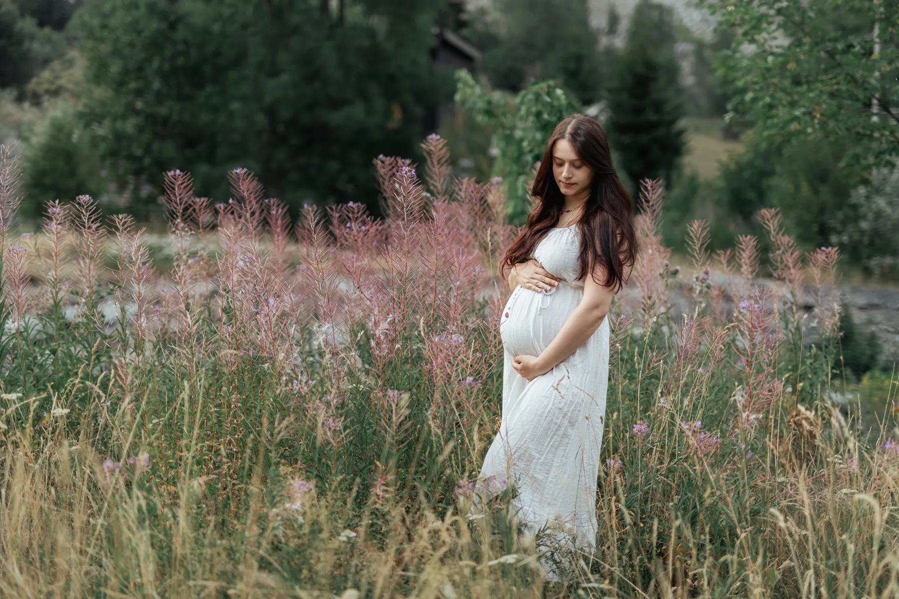 Donna in gravidanza con abito bianco fotografata tra i fiori in montagna