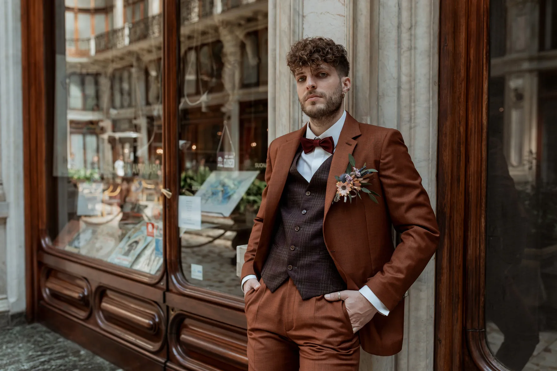 Fotografia fashion uomo in abito marrone Modello con completo marrone fotografato davanti a una vetrina durante un servizio fashion