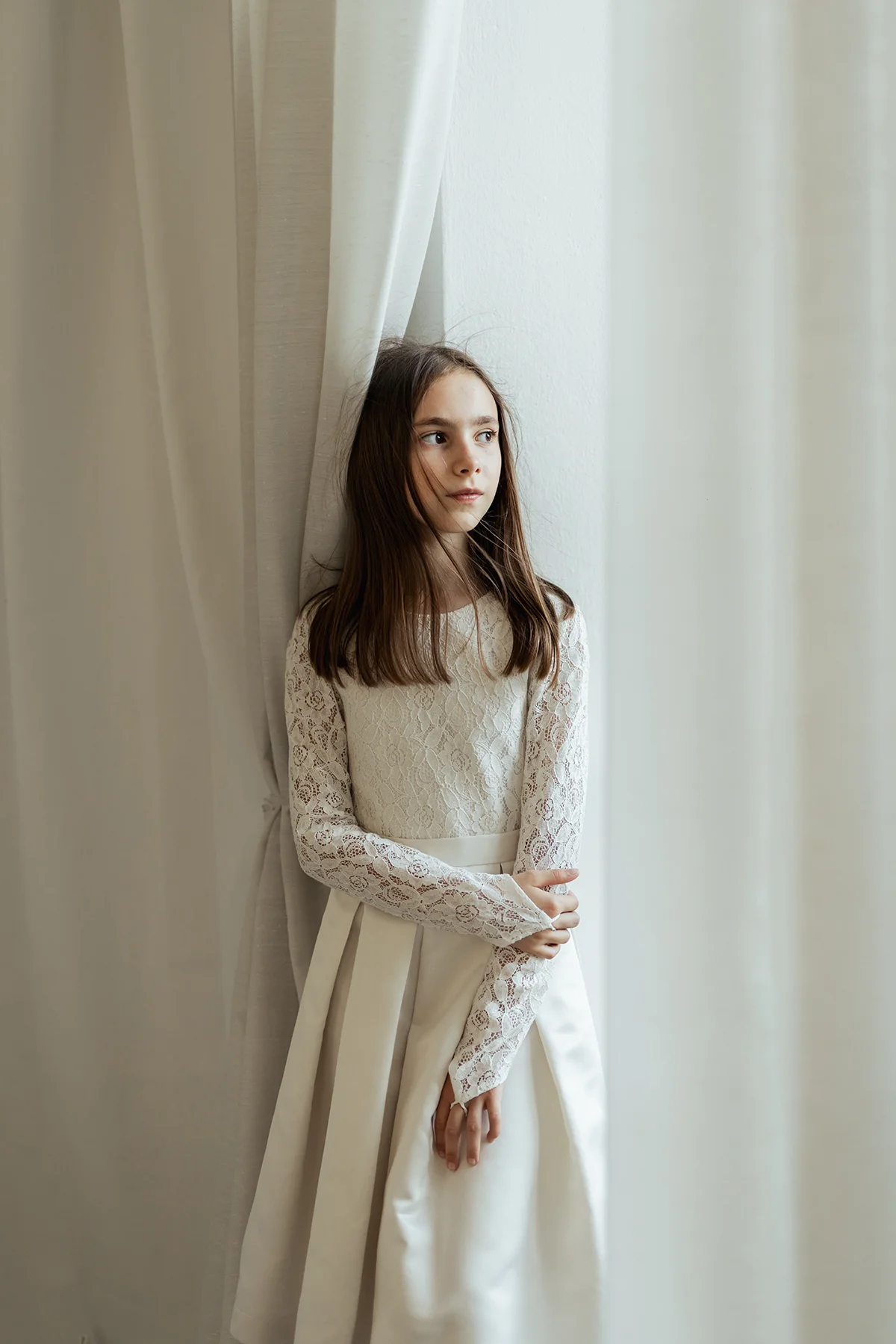 Ragazza fotografata tra tende bianche illuminate dalla luce naturale