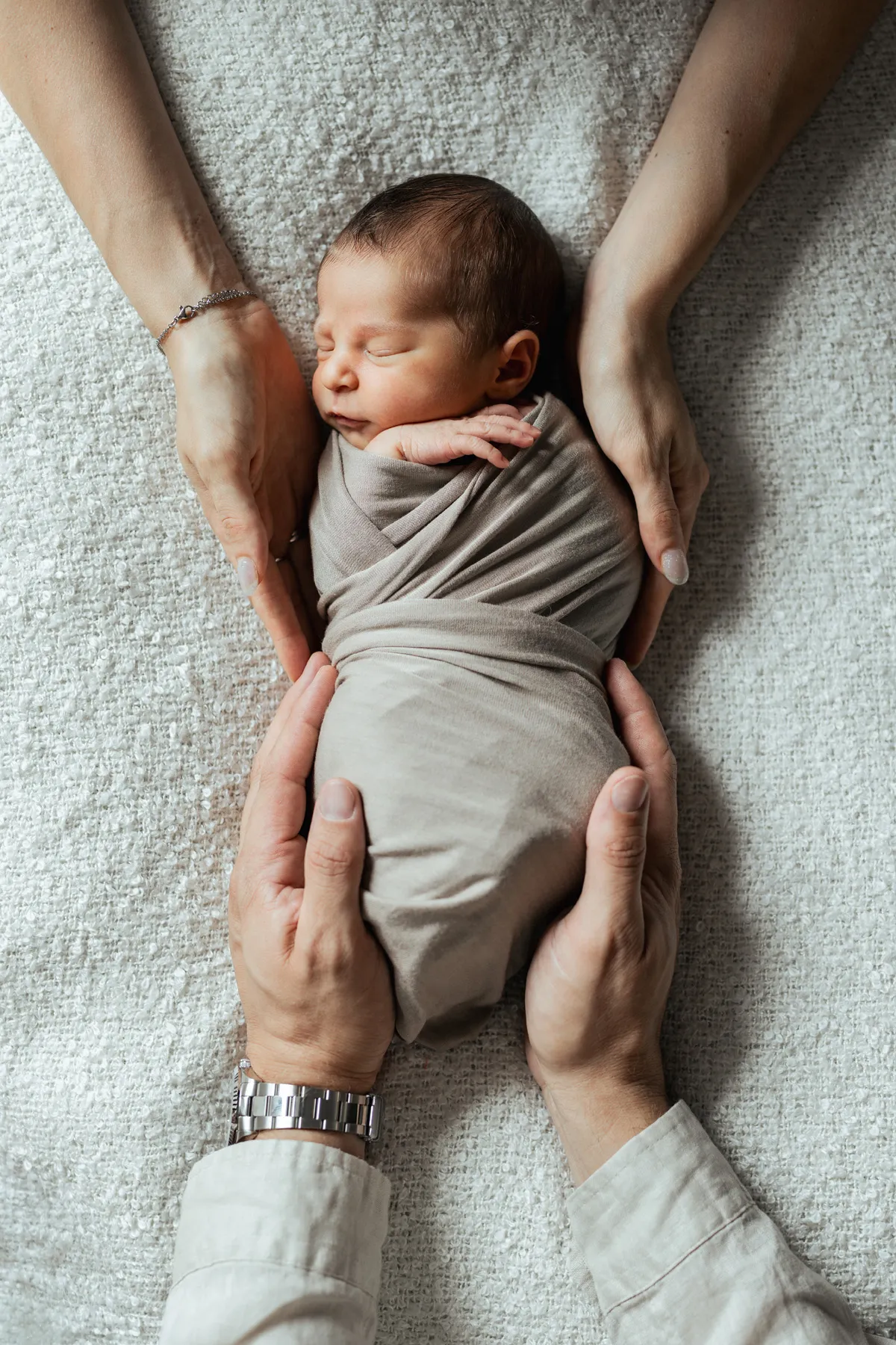 Neonato addormentato circondato dalle mani dei genitori